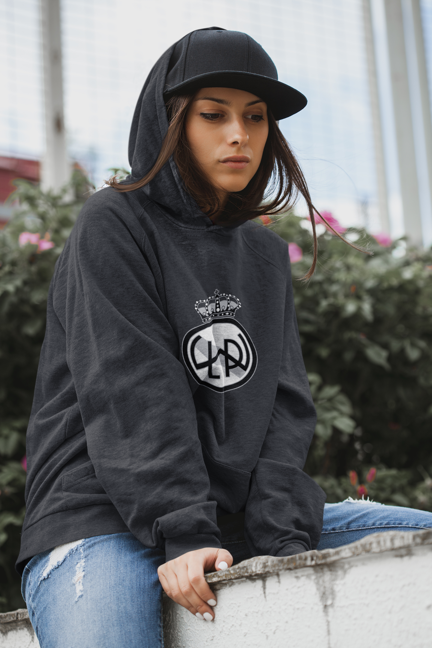 A young women sitting on a wall wearing a dark gray hoodies with the Lake Washington Premier FC club crest on the front in black and white.