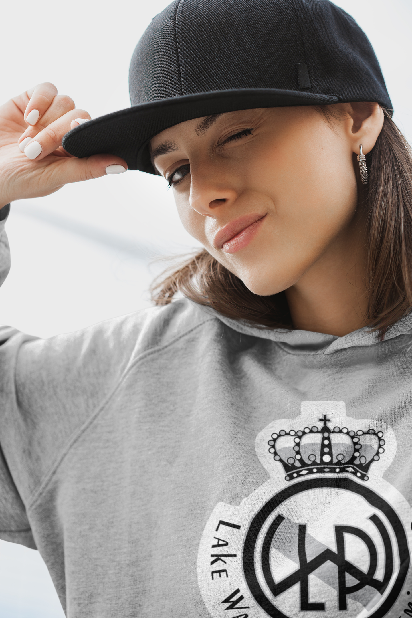 A young girl smiling and wearing and black baseball hat and a gray Lake Washington Premier FC Hoodie with the club crest on the front in black and white colors.