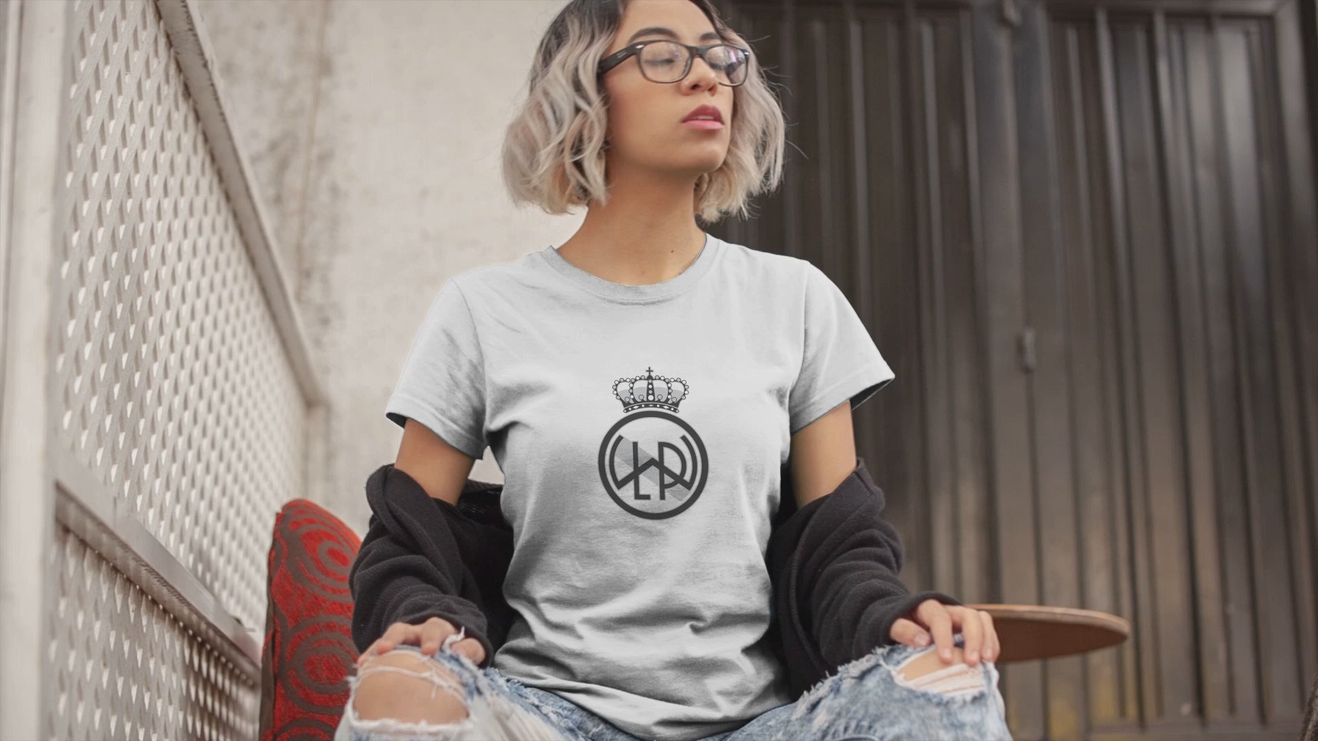 Load video: A t-shirt video featuring an edgy woman with blue framed glasses and short colored hair wearing an LWPFC dark gray short sleeved t-shirt with the club logo in black and white.